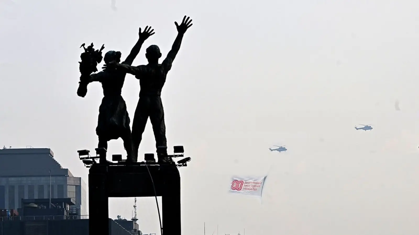 Siluet Patung Selamat Datang dengan helikopter membawa bendera